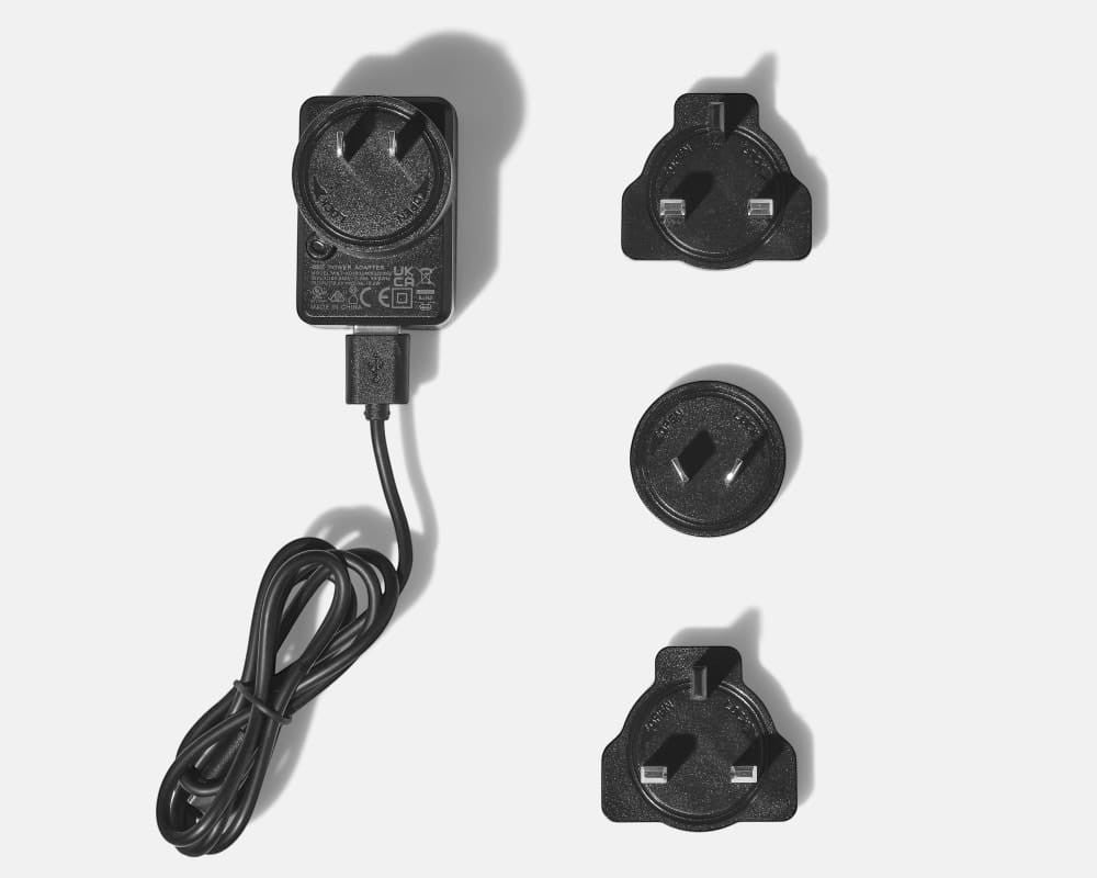 BirdieBox Gravity Move Heated Mini Massager charger with USB cable and three interchangeable plug adapters for travel.