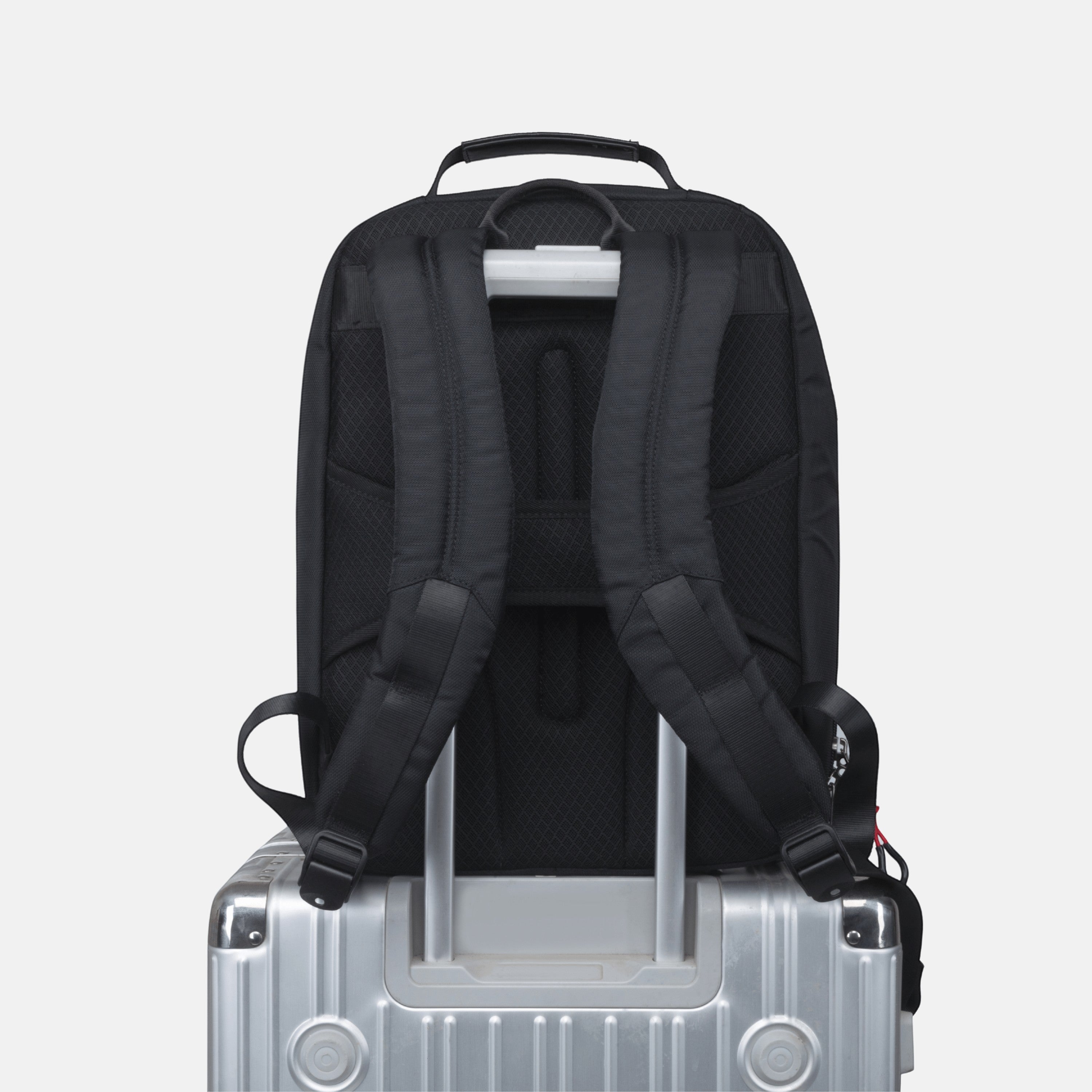 BirdieBox Hudson Cole Prospect black backpack with adjustable straps and luggage sleeve, shown on a silver suitcase.