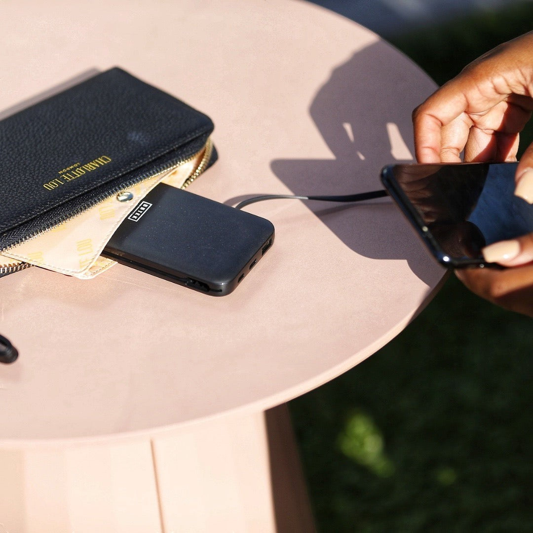BirdieBox Charlotte Lou black vegan leather clutch with interior organization and BB-Tek wireless power bank, a hand charges a phone.