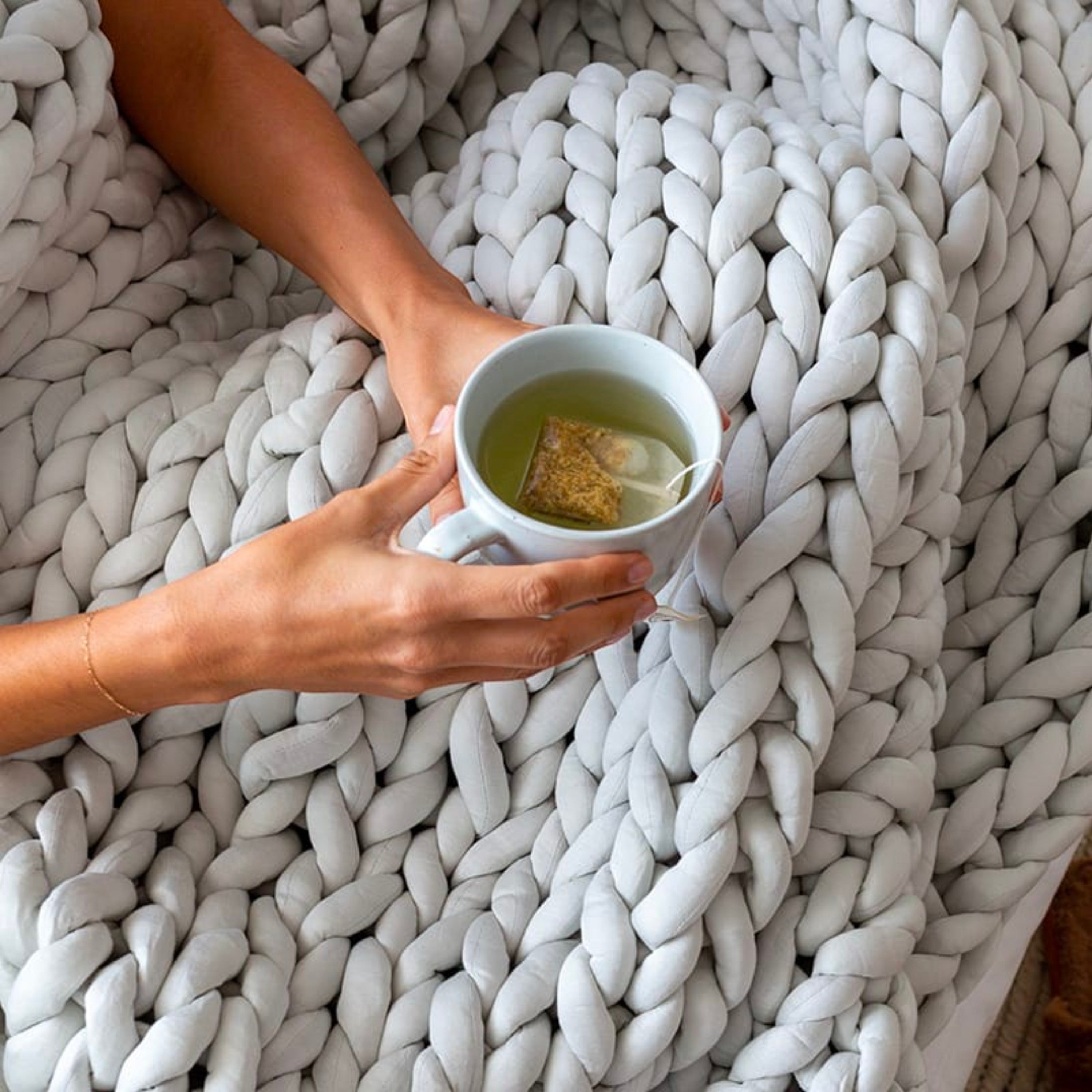 BirdieBox light grey chunky knit bamboo jersey weighted blanket held by a person drinking tea.