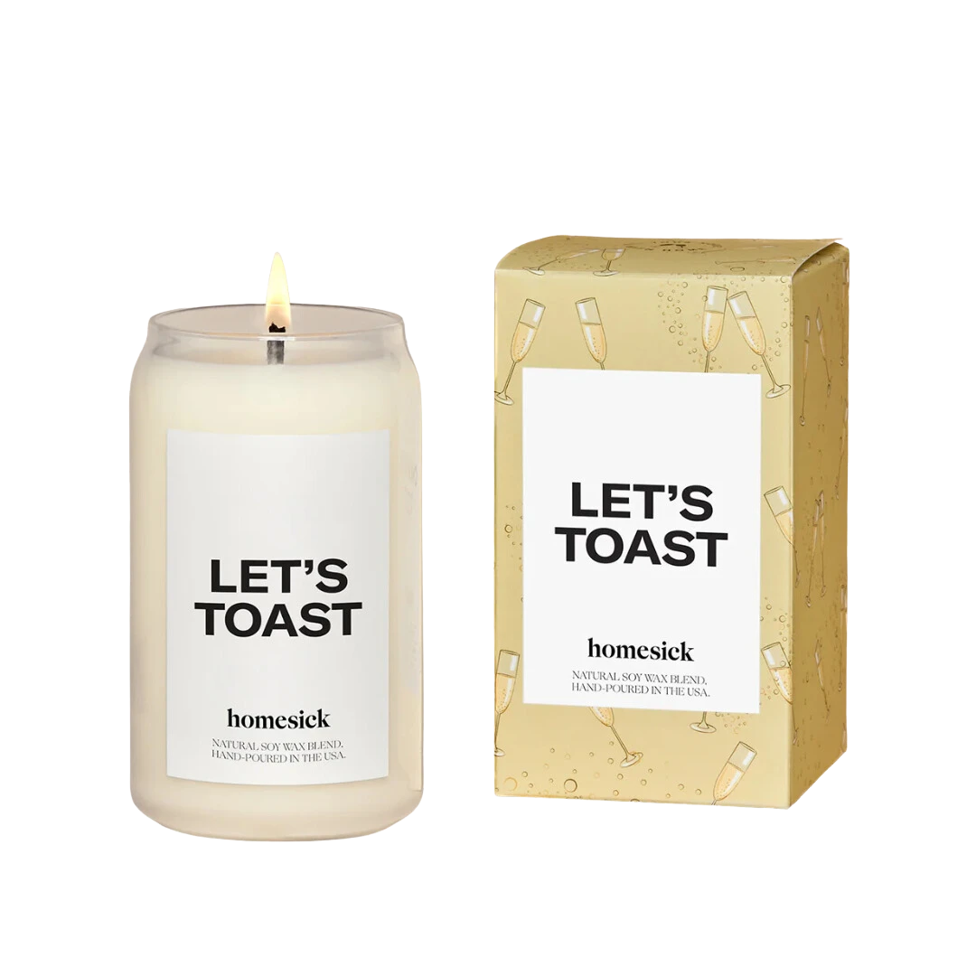 BirdieBox Homesick Let's Toast candle in a clear glass jar with a white label and lit wick. Box features champagne glasses.