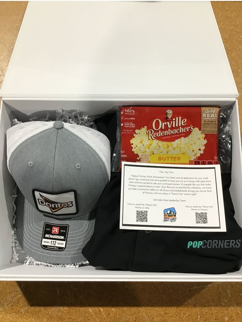 BirdieBox white gift box containing a grey Doritos trucker hat, a box of Orville Redenbacher's butter popcorn, and a black Popcorners shirt with a note.